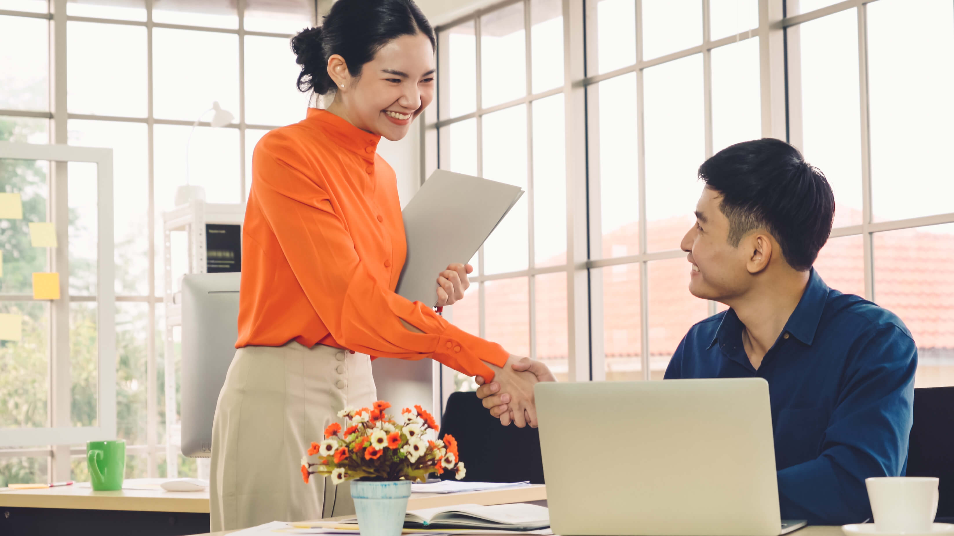 smiling woman shaking man's hand next to desk with laptop