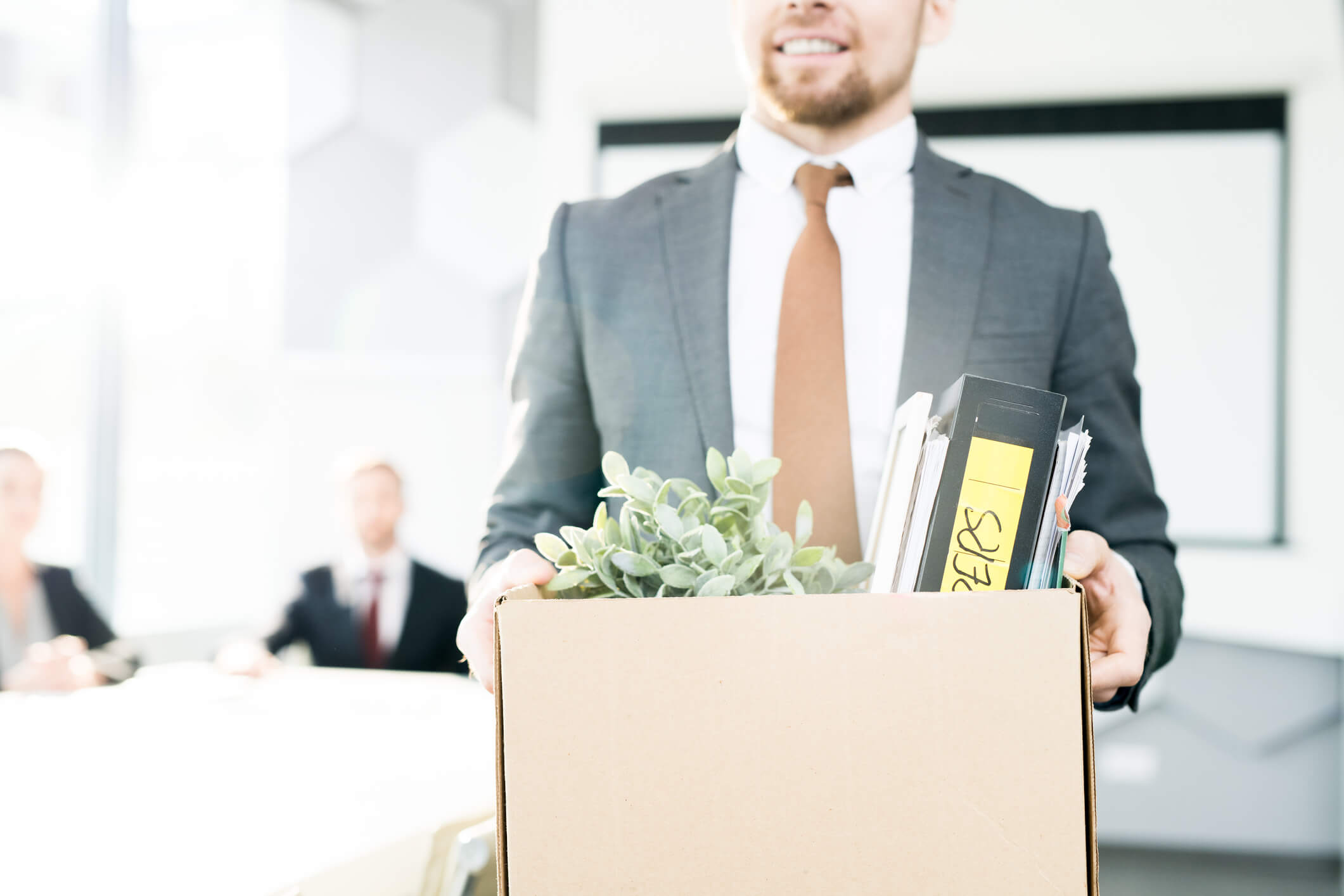 man in suit smiling with box of office items during the great resignation